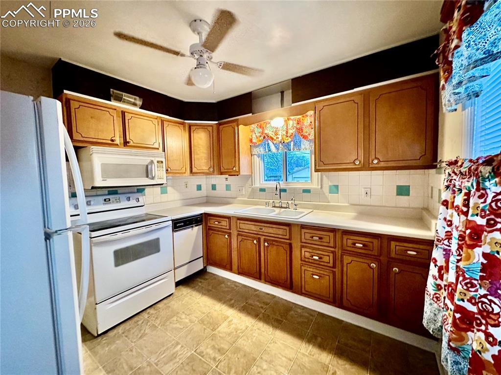 Kitchen with white appliances, light countertops, a ceiling fan, brown cabinetry, and decorative backsplash