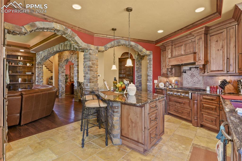 Kitchen with light wood-type flooring, pendant lighting, stainless steel gas cooktop, a breakfast bar area, and ornamental molding