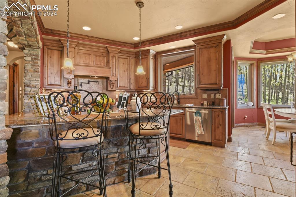 Kitchen with a tray ceiling, crown molding, stainless steel dishwasher, pendant lighting, and light tile floors