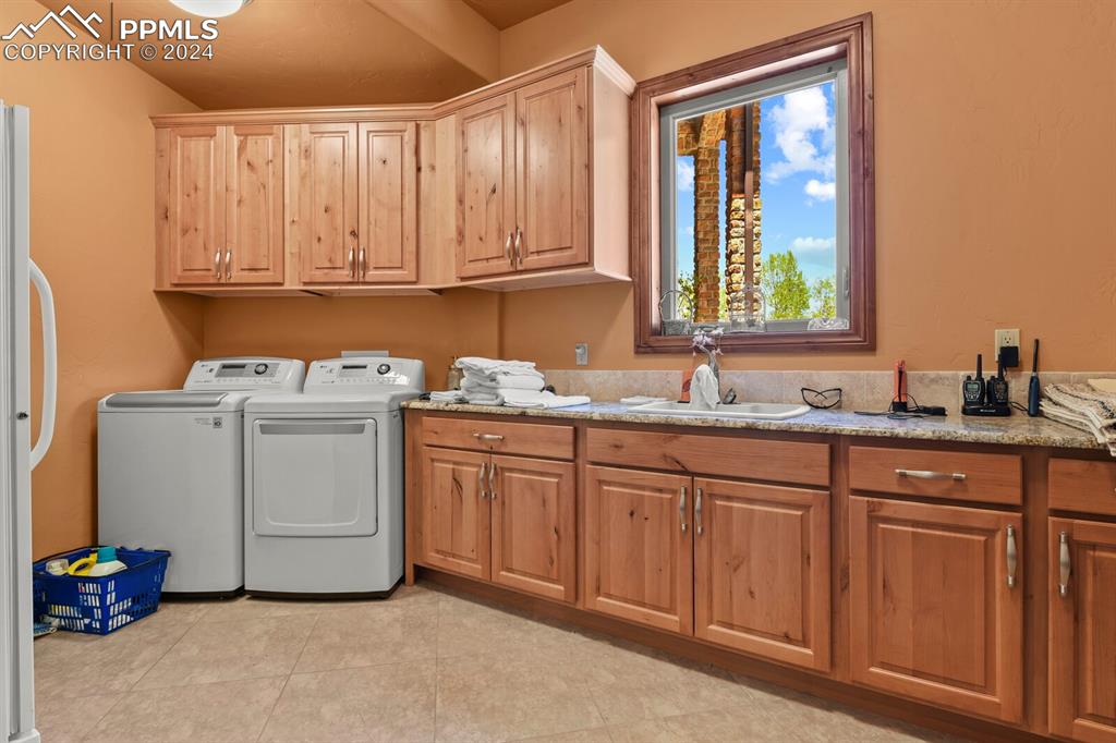Laundry area with cabinets, sink, light tile floors, and washing machine and clothes dryer
