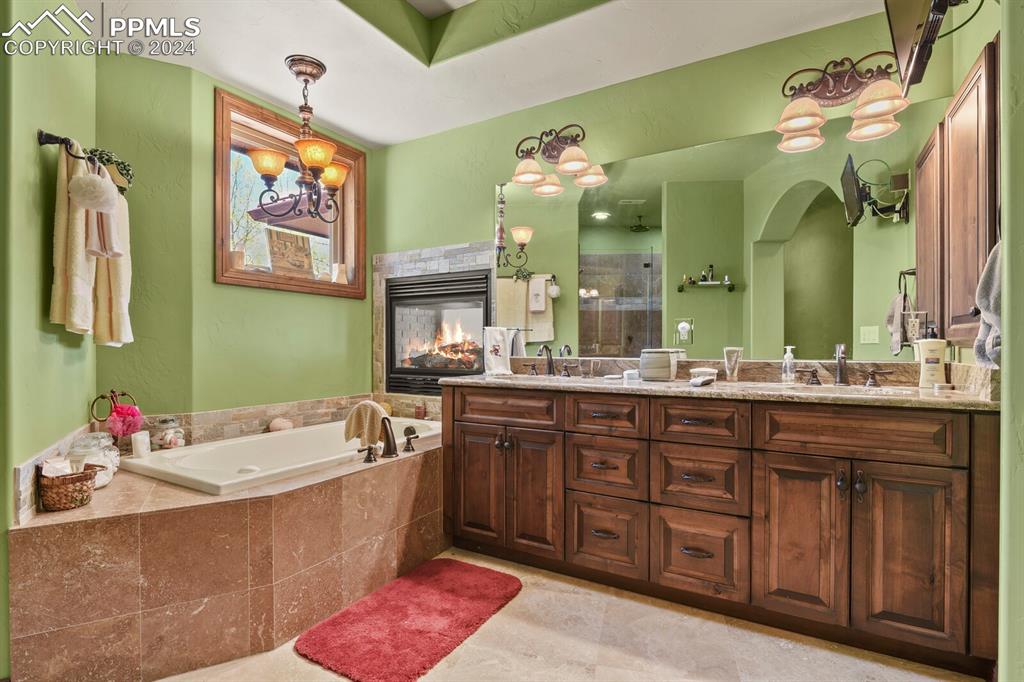 Bathroom with dual vanity, an inviting chandelier, tile floors, a multi sided fireplace, and tiled bath