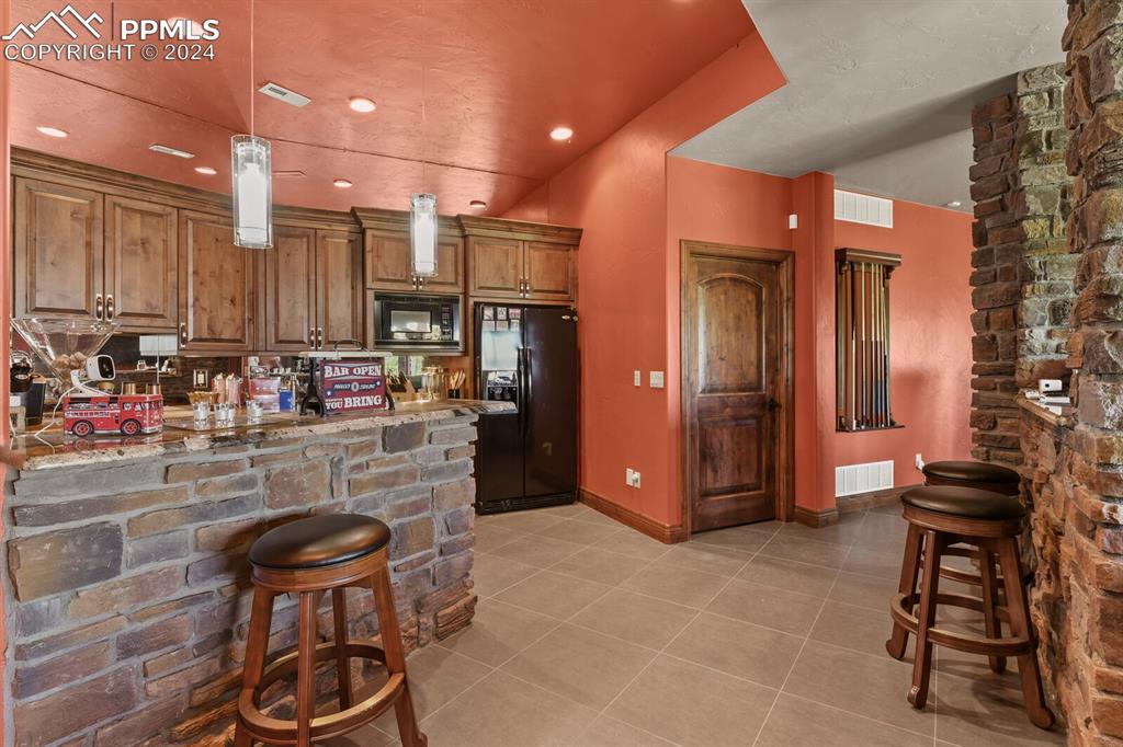 Kitchen featuring light stone counters, black appliances, light tile floors, and pendant lighting