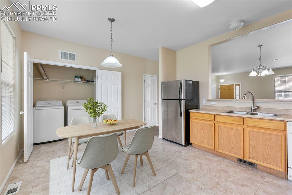 *Virtually Staged* Kitchen featuring washing machine and clothes dryer, freestanding refrigerator, a chandelier, decorative light fixtures, and light countertops
