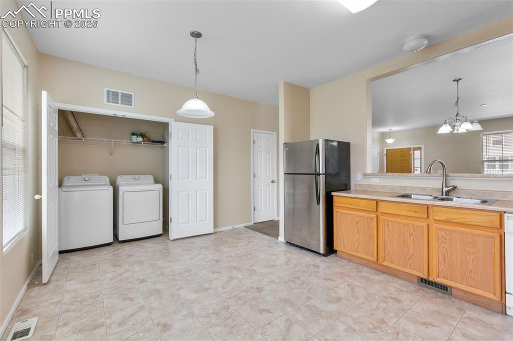 Kitchen featuring freestanding refrigerator, a chandelier, separate washer and dryer, light countertops, and decorative light fixtures