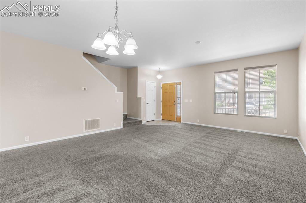 Unfurnished living room with carpet flooring, stairway, and a chandelier