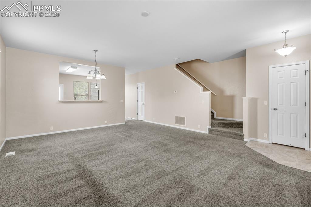 Unfurnished living room with carpet flooring, stairs, and a chandelier