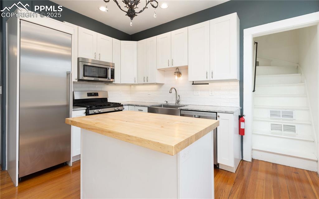 Kitchen featuring wooden counters, backsplash, stainless steel appliances, light wood finished floors, and white cabinets
