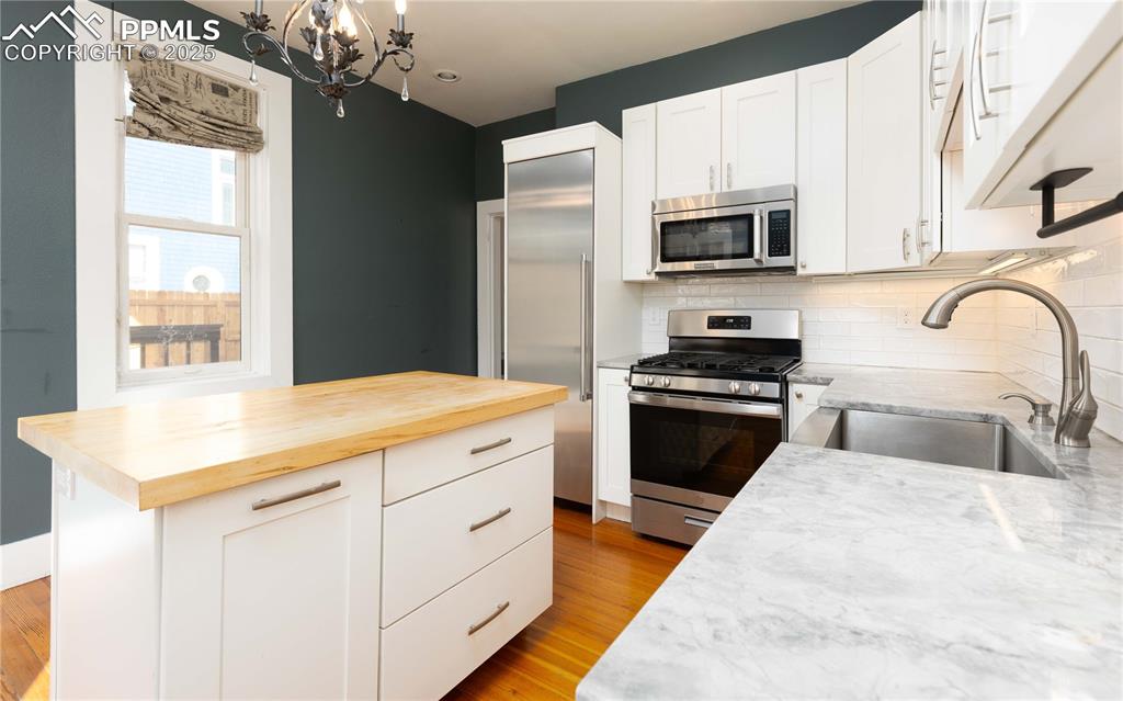 Kitchen with stainless steel appliances, white cabinets, wooden counters, and decorative backsplash