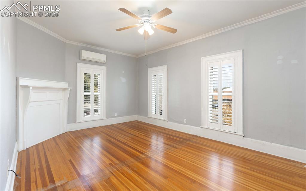 Empty room with wood finished floors, crown molding, ceiling fan, and a wall unit AC