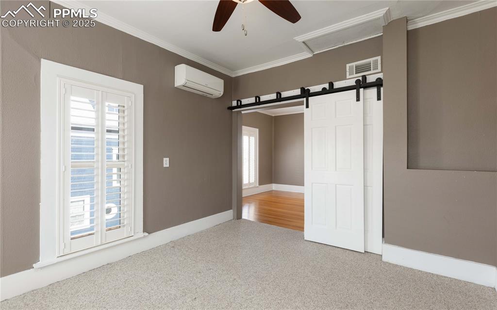 Unfurnished room with ceiling fan, carpet, a barn door, ornamental molding, and a wall mounted air conditioner