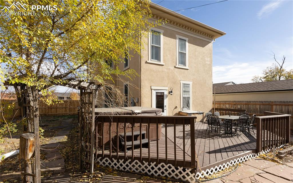 Rear view of house featuring a fenced backyard, stucco siding, outdoor dining area, and a deck