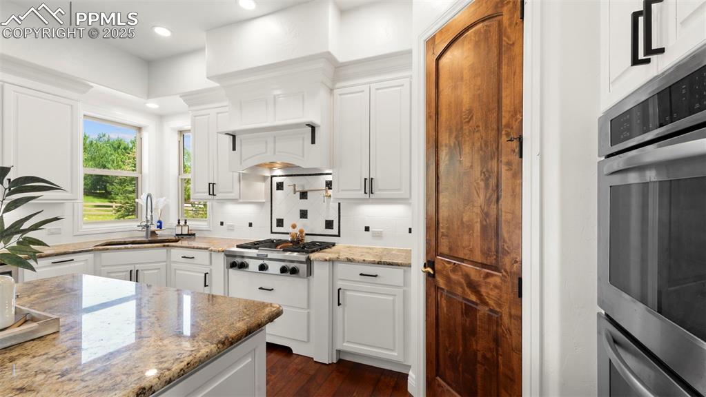 Kitchen with white cabinets, light stone countertops, decorative backsplash, dark wood finished floors, and recessed lighting