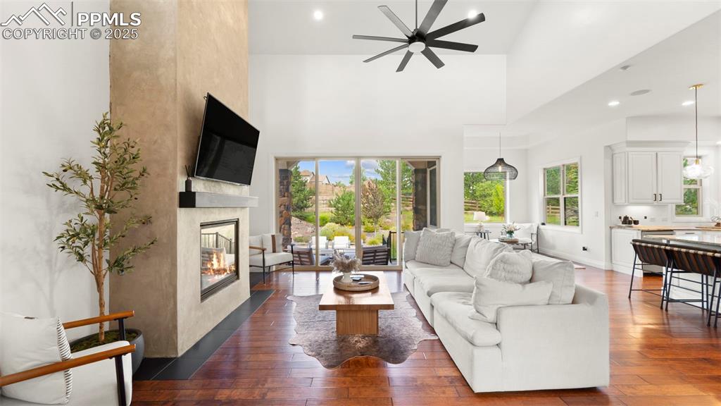 Living room with a towering ceiling, dark wood finished floors, healthy amount of natural light, a glass covered fireplace, and recessed lighting