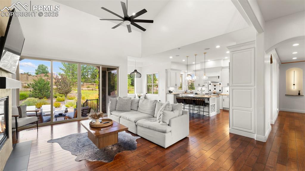 Living room featuring arched walkways, a high ceiling, dark wood finished floors, a glass covered fireplace, and recessed lighting