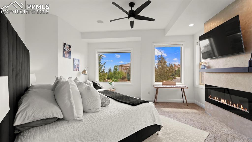 Bedroom with light colored carpet, recessed lighting, a glass covered fireplace, and a ceiling fan