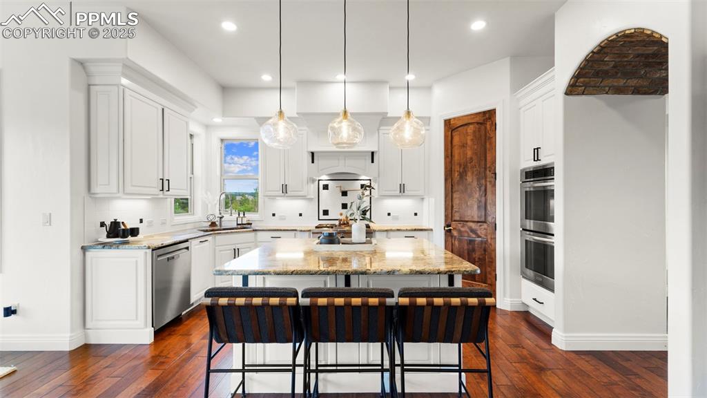 Kitchen with a kitchen island, a kitchen bar, decorative light fixtures, light stone countertops, and white cabinets