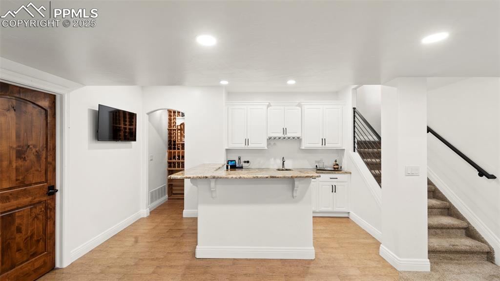 Kitchen featuring light stone counters, white cabinets, recessed lighting, a breakfast bar area, and light wood-style flooring