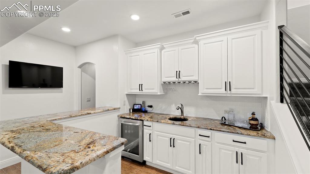 Kitchen featuring decorative backsplash, light stone counters, white cabinetry, wine cooler, and recessed lighting