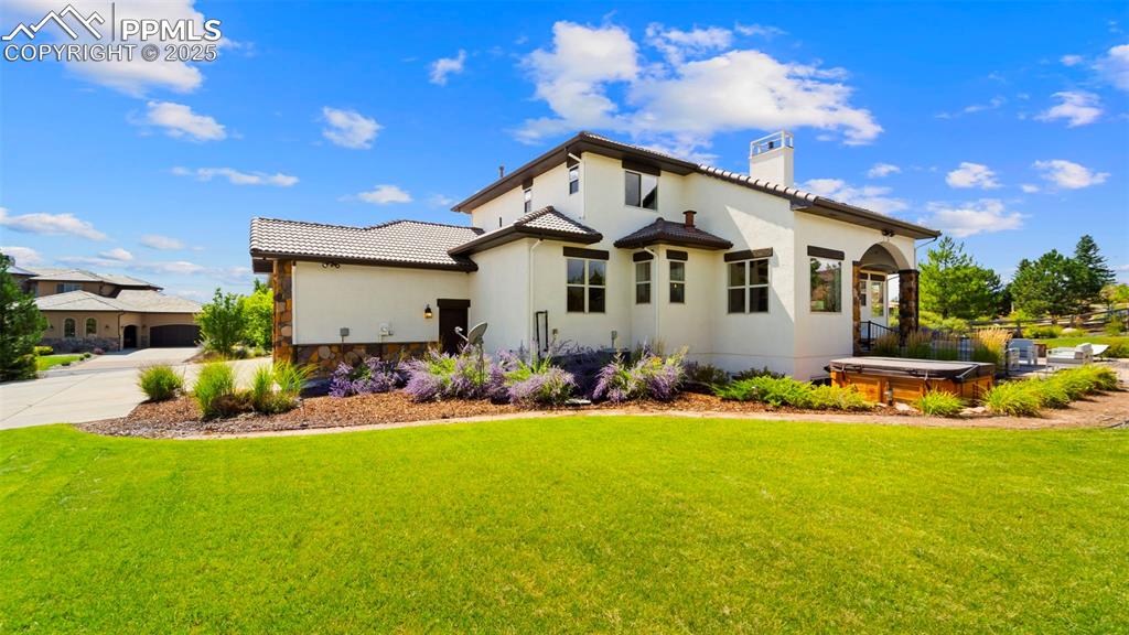 Mediterranean / spanish-style house with a chimney, a hot tub, stucco siding, and a front lawn