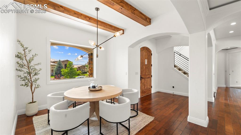 Dining area with a chandelier, dark wood-type flooring, stairway, beam ceiling, and arched walkways