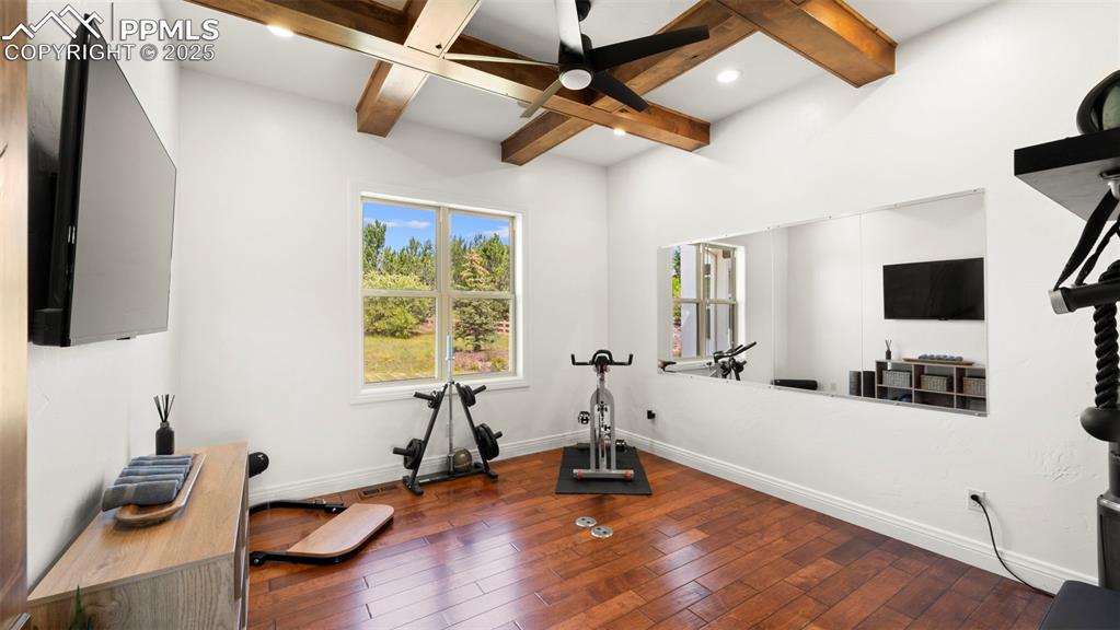 Exercise area with dark wood finished floors, a ceiling fan, and coffered ceiling