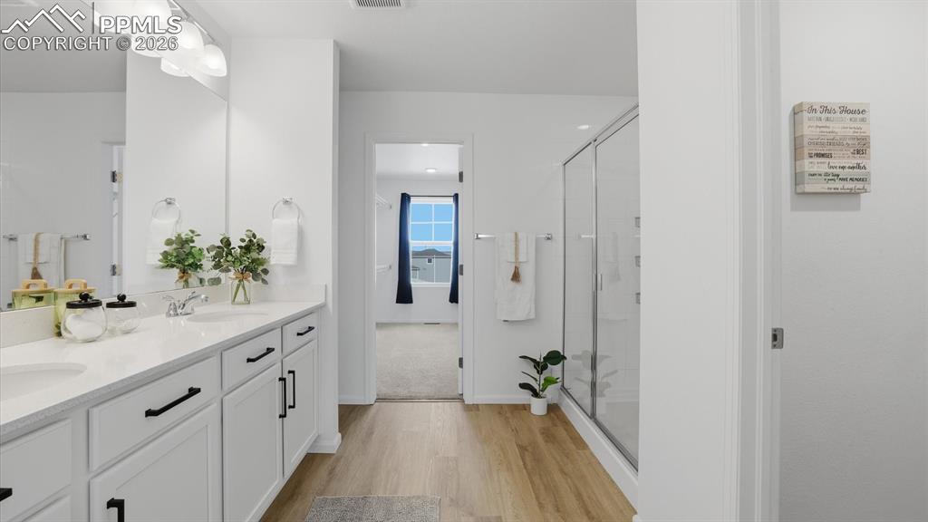 Upper Level Primary Bathroom with dual sink vanity, mirror, luxury vinyl plank flooring and enclosed tiled shower.