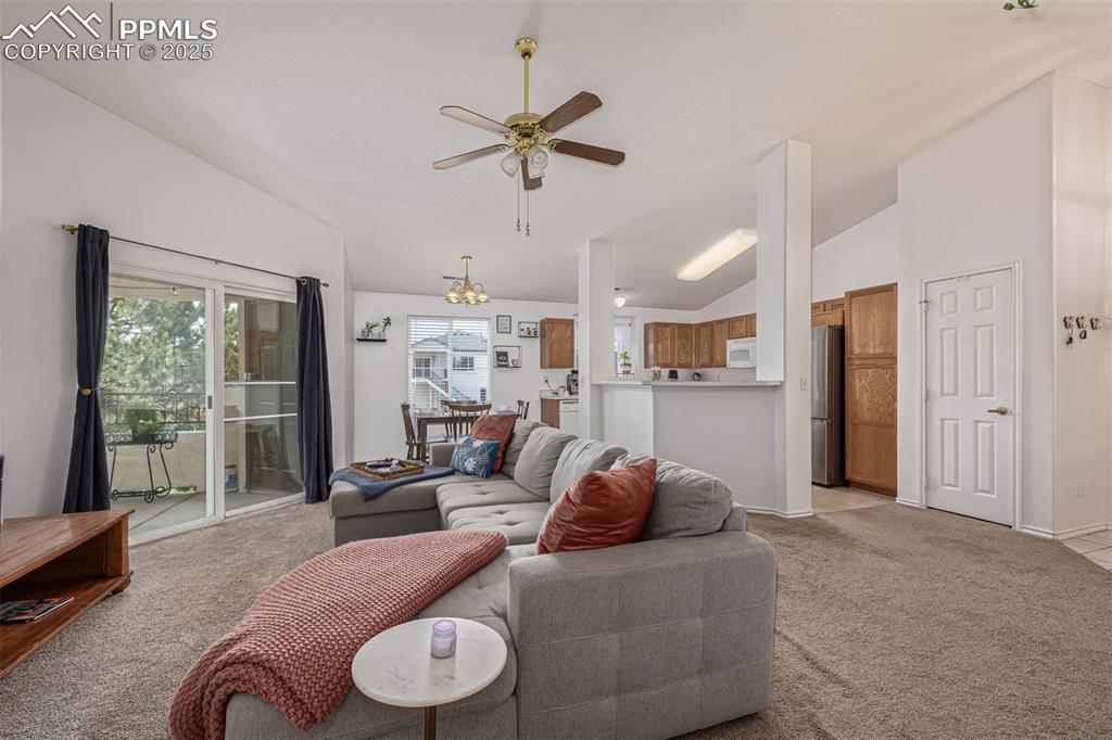 Living room featuring lofted ceiling, light carpet, ceiling fan, and a chandelier