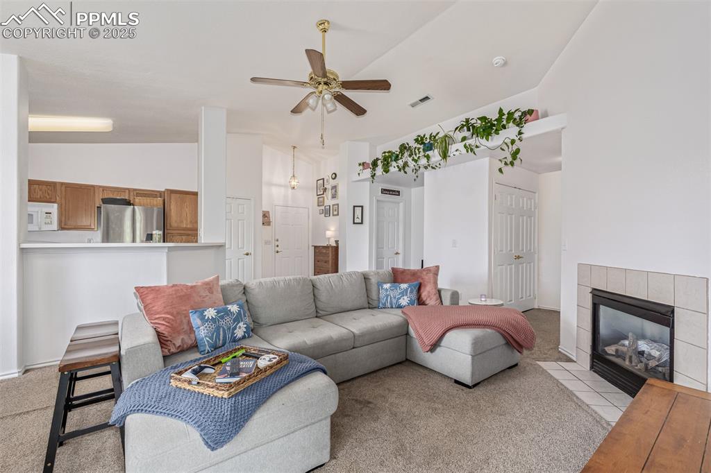 Living area with a ceiling fan, a fireplace, light colored carpet, and high vaulted ceiling