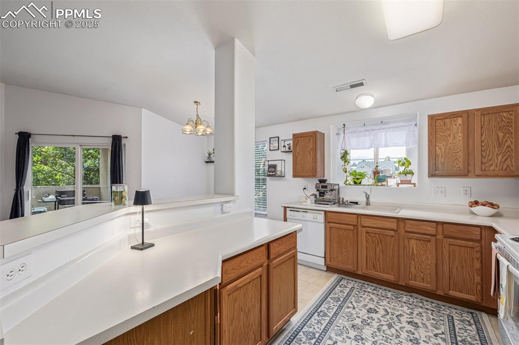 Kitchen featuring light countertops, brown cabinetry, white appliances, hanging light fixtures, and a chandelier