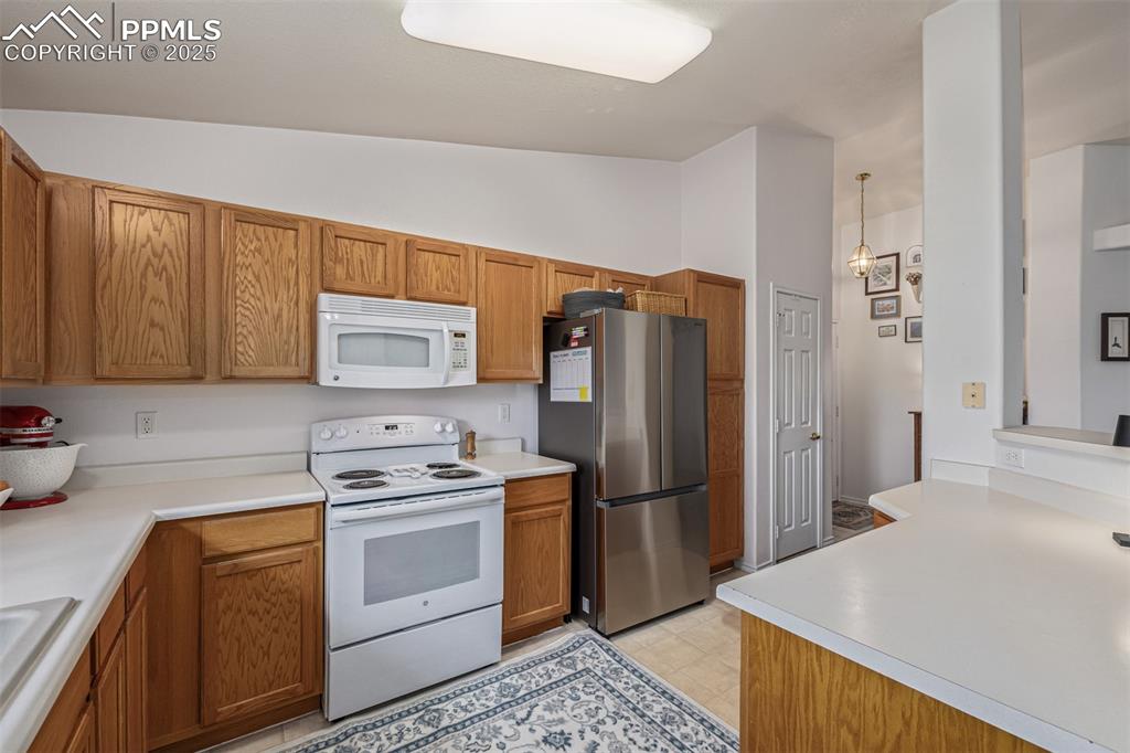 Kitchen with white appliances, brown cabinets, light countertops, and lofted ceiling
