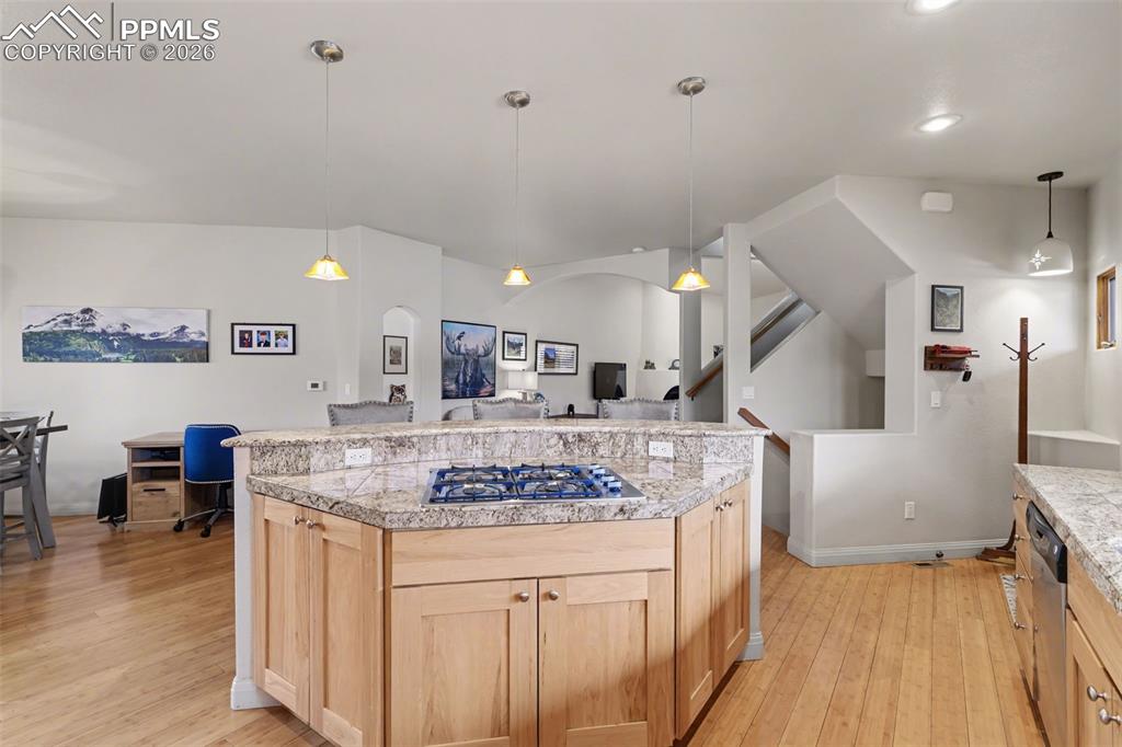 Kitchen with light wood finish cabinetry, open floor plan, a breakfast bar area, light stone countertops, and freestanding refrigerator