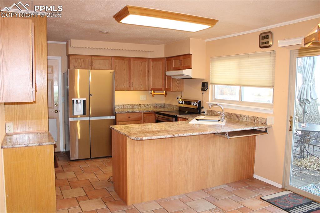 Kitchen with stainless steel appliances, a peninsula, crown molding, light stone countertops 