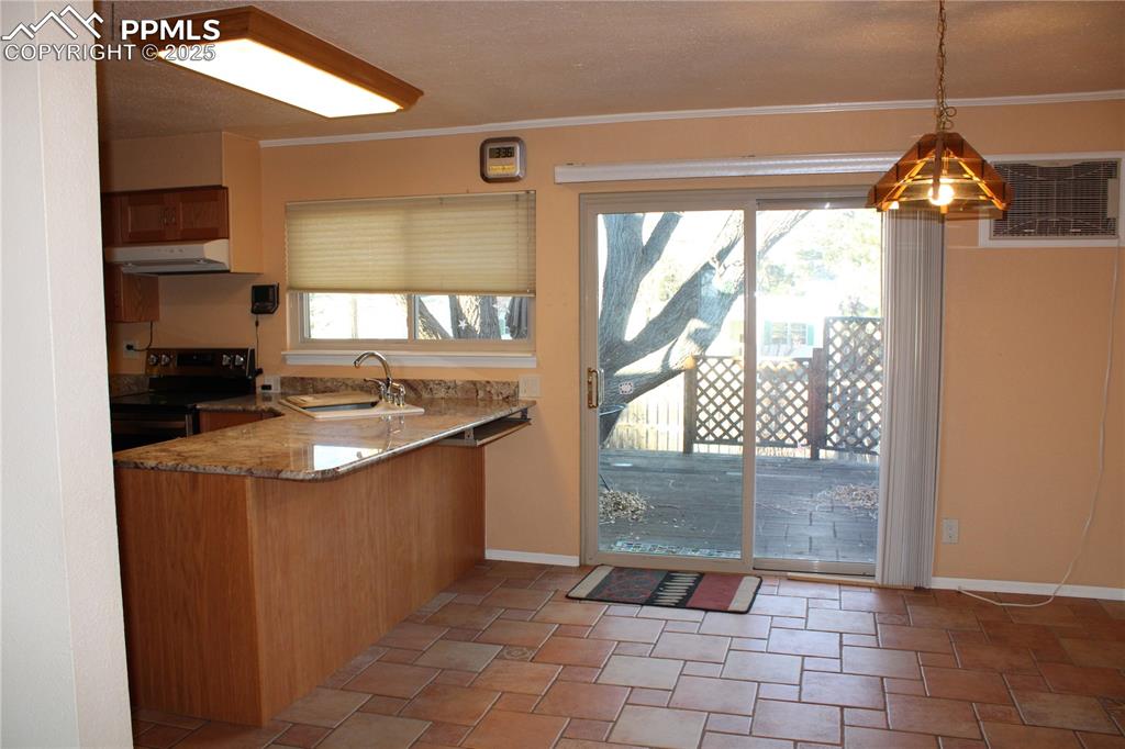Kitchen with electric stove, light stone counters, pendant lighting, under cabinet range hood, and a peninsula