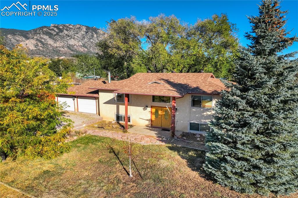 View of front of house with stucco siding, roof with shingles, a garage, and a mountain view