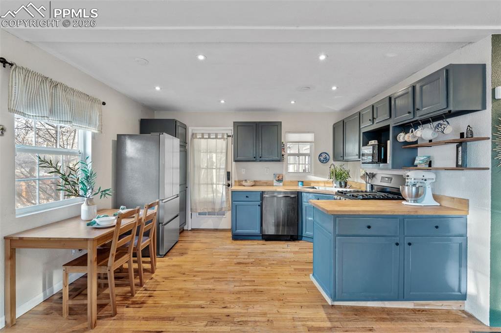 Kitchen with stainless steel appliances, open shelves, wooden counters, light wood-style flooring, and recessed lighting