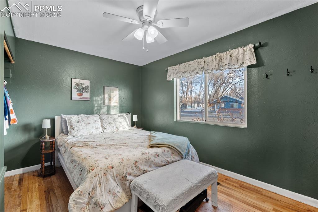 Bedroom with a textured wall, wood finished floors, and ceiling fan
