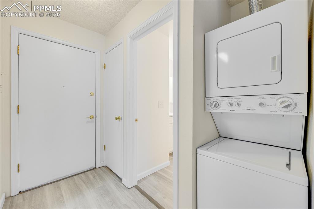 Laundry area with a textured ceiling, stacked washer / dryer, and light wood-type flooring