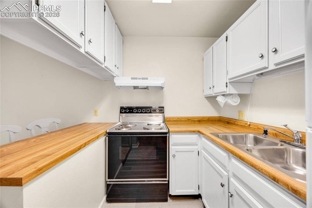 Kitchen with electric range oven, white cabinetry, and under cabinet range hood
