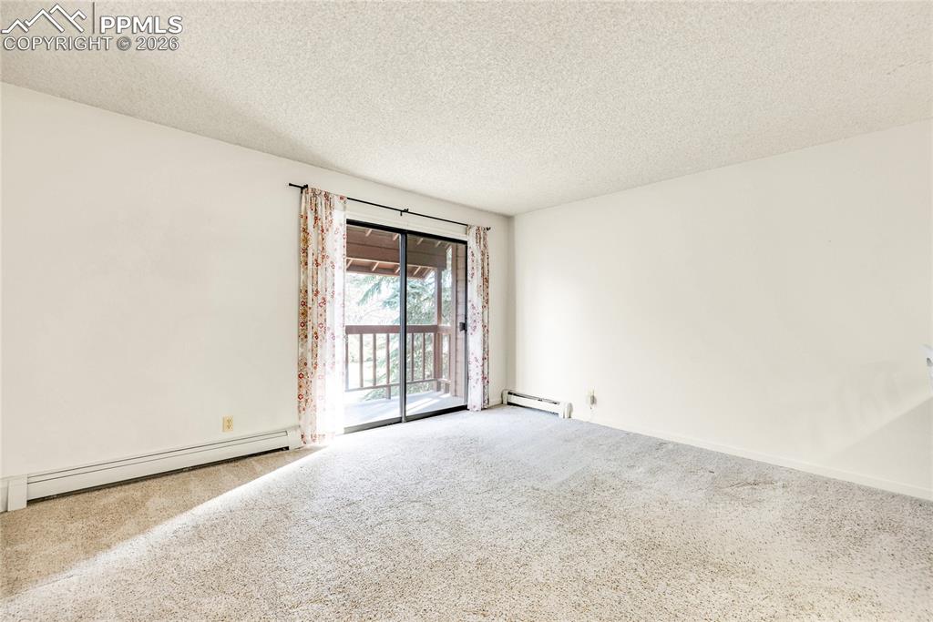 Carpeted empty room featuring a textured ceiling and a baseboard heating unit