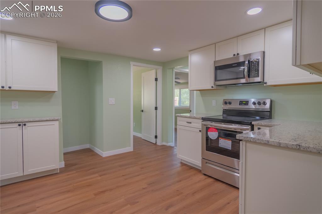 Kitchen with stainless steel appliances, light stone counters, light wood-type flooring, white cabinetry, and recessed lighting