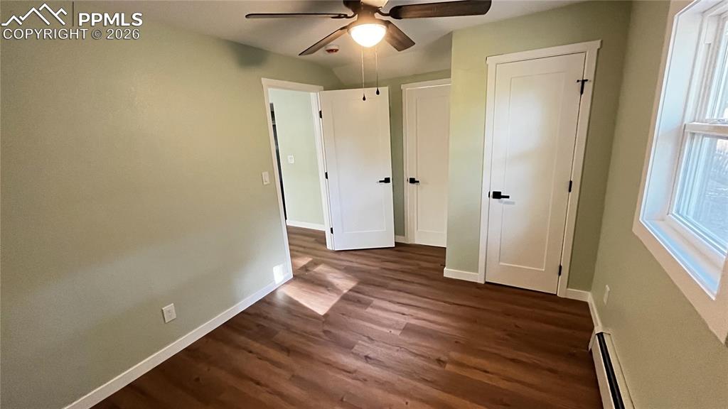 Unfurnished main  bedroom with attached bathroom with dark wood-style flooring, a baseboard heating unit, and a ceiling fan