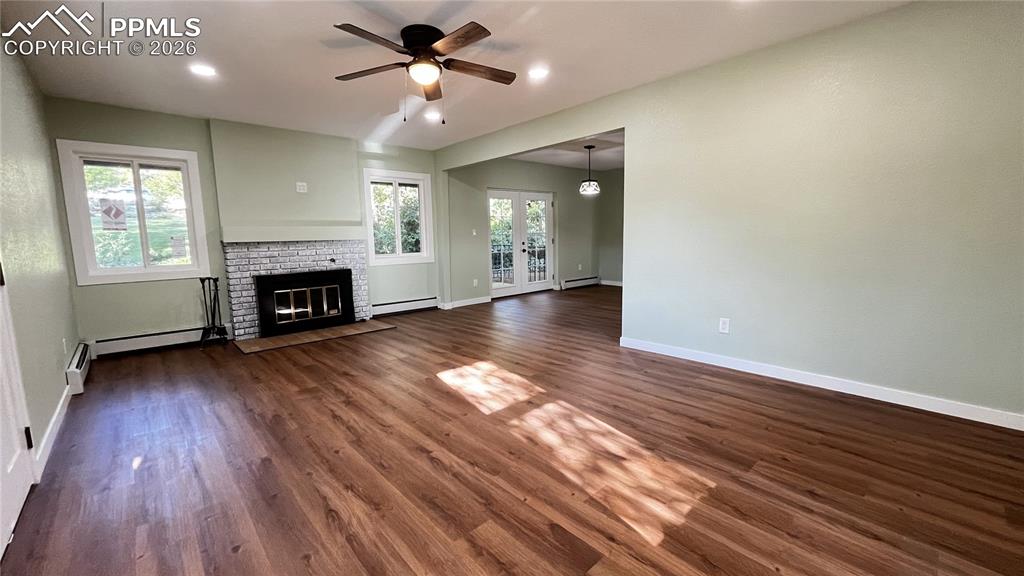 Unfurnished living room with french doors, dark wood finished floors, ceiling fan, a brick fireplace, and baseboard heating