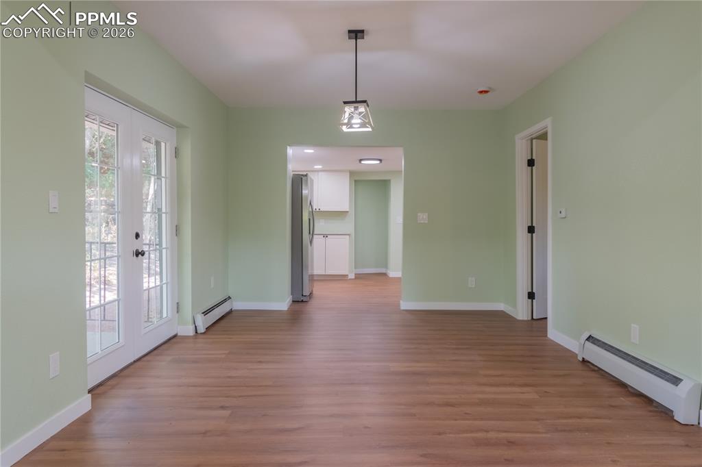Unfurnished dining area featuring baseboard heating, light wood-style floors, and french doors