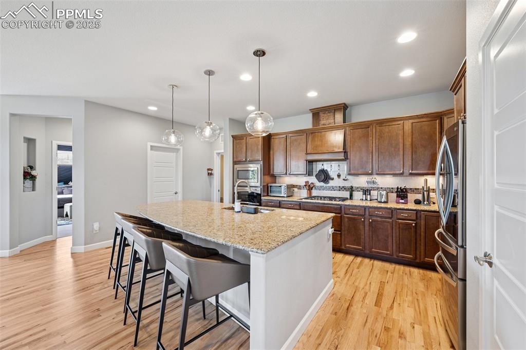 Kitchen with appliances with stainless steel finishes, recessed lighting, a kitchen island with sink, light wood finished floors, and light stone counters