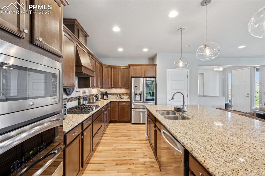 Kitchen featuring stainless steel appliances, light wood-style floors, light stone counters, pendant lighting, and tasteful backsplash