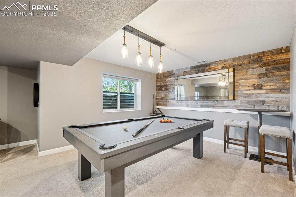Game room with carpet flooring, pool table, wooden walls, and a textured ceiling