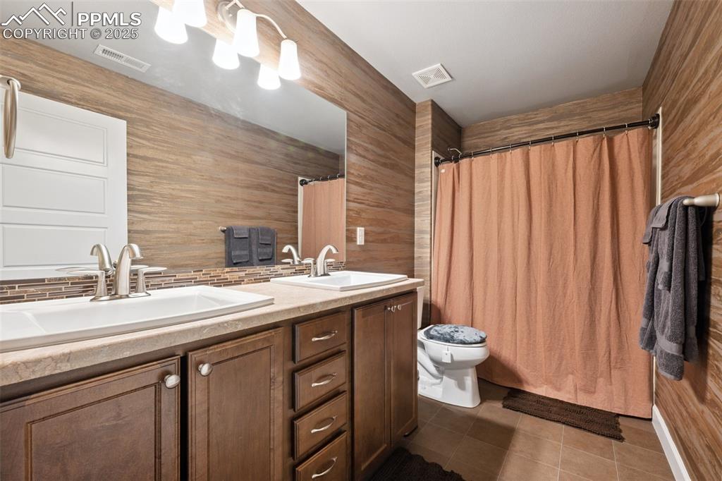 Full bathroom with tasteful backsplash, double vanity, tile patterned floors, and curtained shower