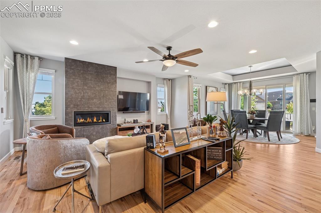 Living room featuring light wood-type flooring, a tiled fireplace, recessed lighting, ceiling fan, and a chandelier