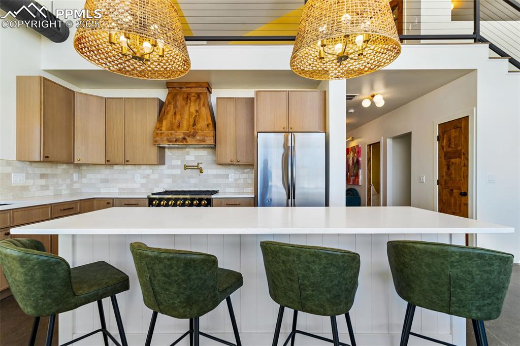 Kitchen featuring a chandelier, freestanding refrigerator, backsplash, and custom exhaust hood