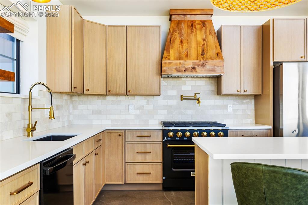 Kitchen featuring light brown cabinets, black appliances, backsplash, and premium range hood